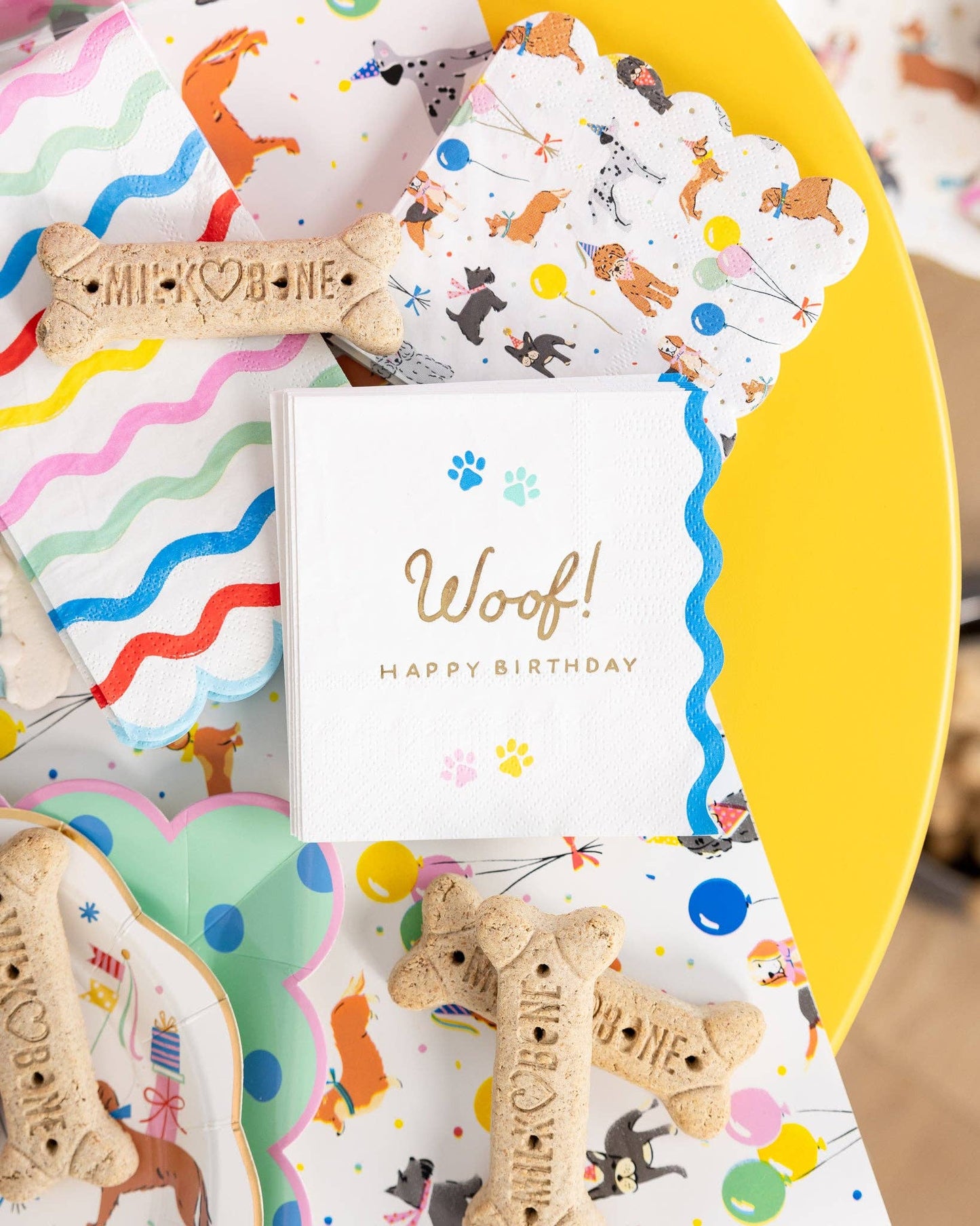 Dog-themed party set up with napkins and treats on a yellow plate