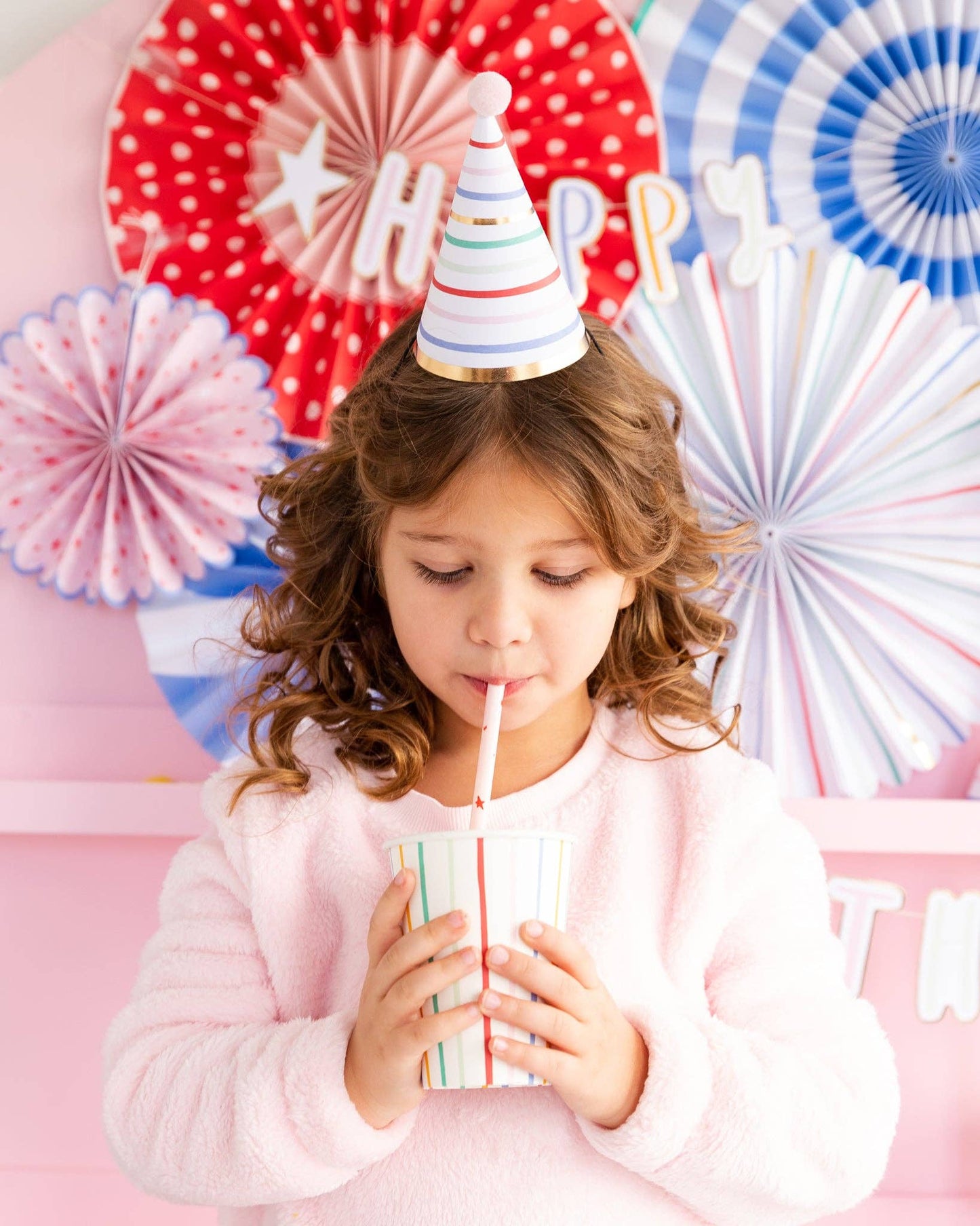 Child celebrating a birthday with colorful decorations and a striped cup.