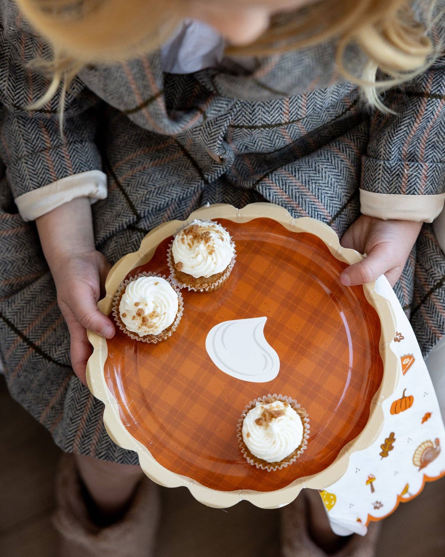 Person holding a plate with cupcakes and a decorative fall-themed napkin.