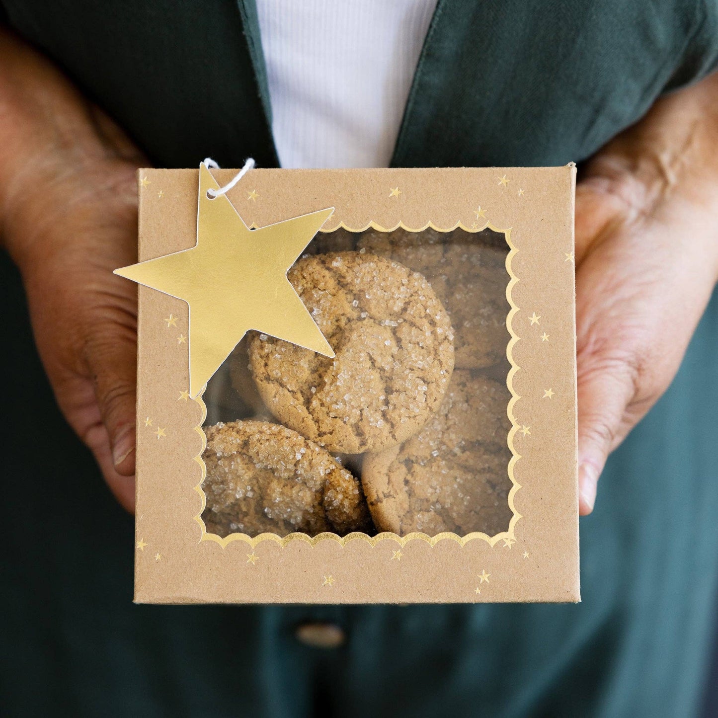 Person holding a box of cookies with a gold star gift tag.