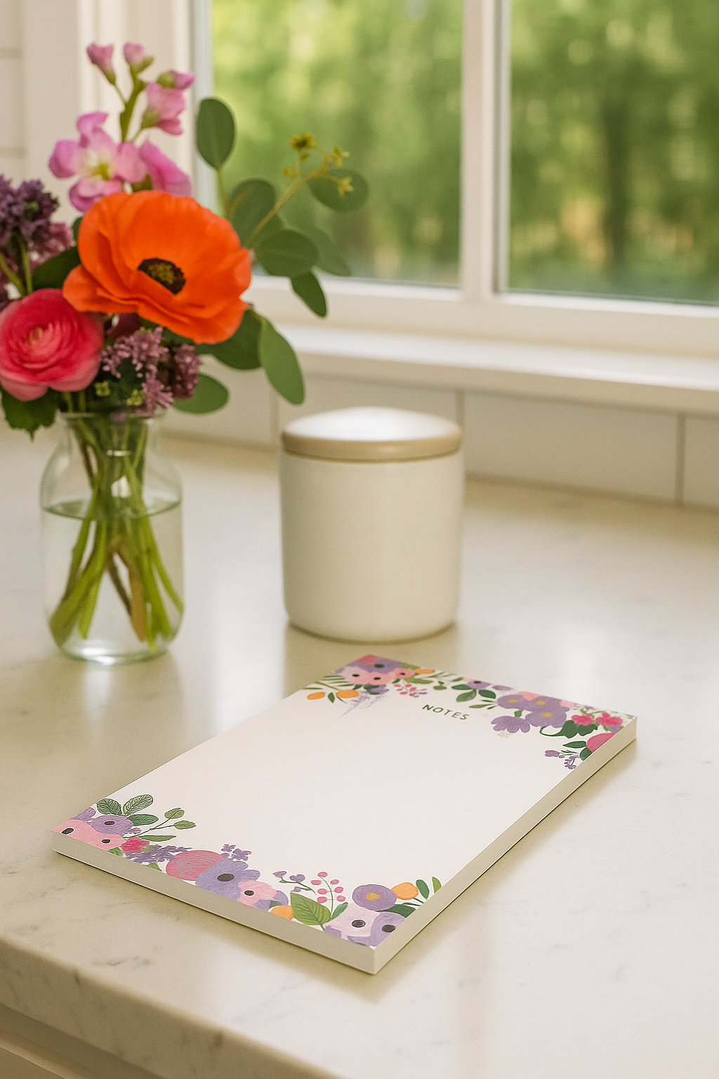 Notebook with floral design on a kitchen counter next to a vase of flowers and a candle.