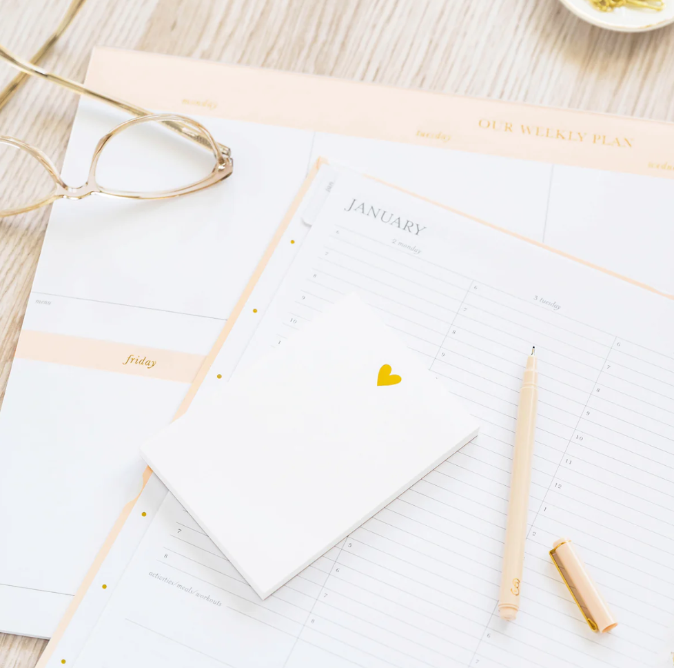 Desk accessories including a calendar open to month of January, a pen and a mini notepad with gold heart on the top