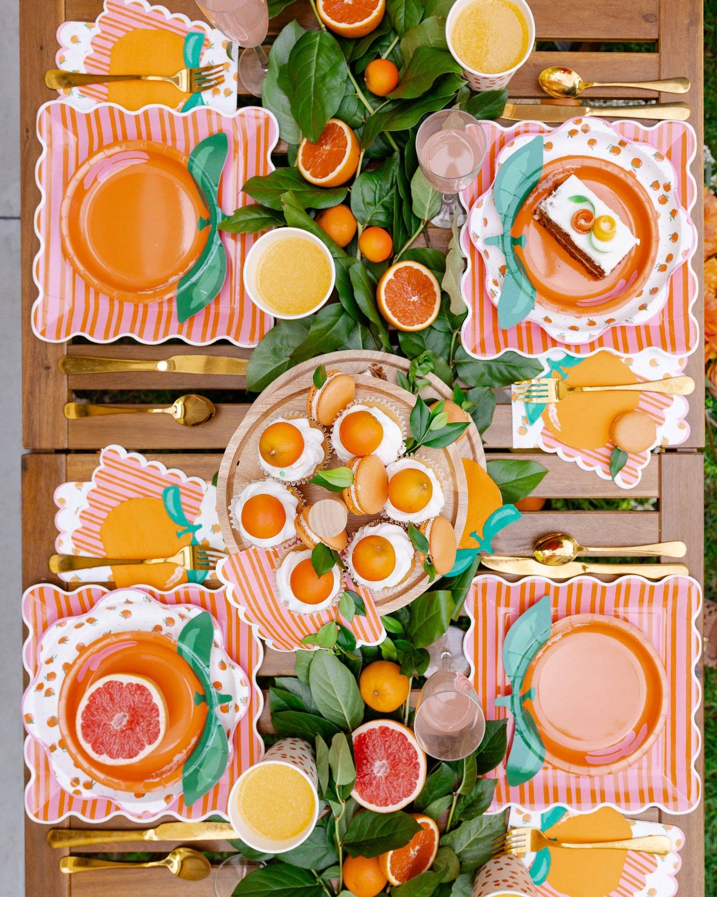 Birds eye view of a citrus-themed tablescape with orange plates, napkins cup and food.
