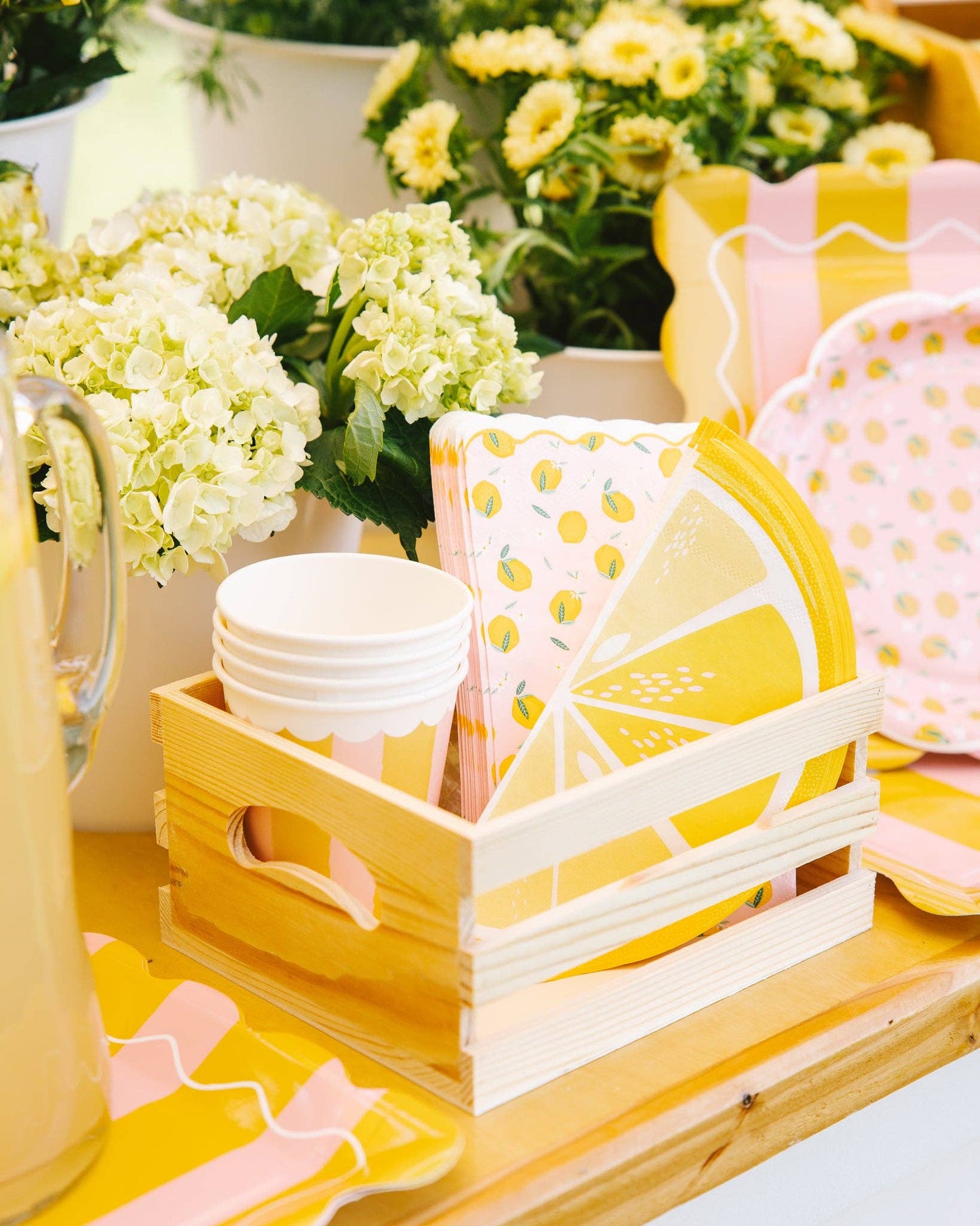 Decorative table setting with lemon-themed plates, cups and napkins in a wooden crate.