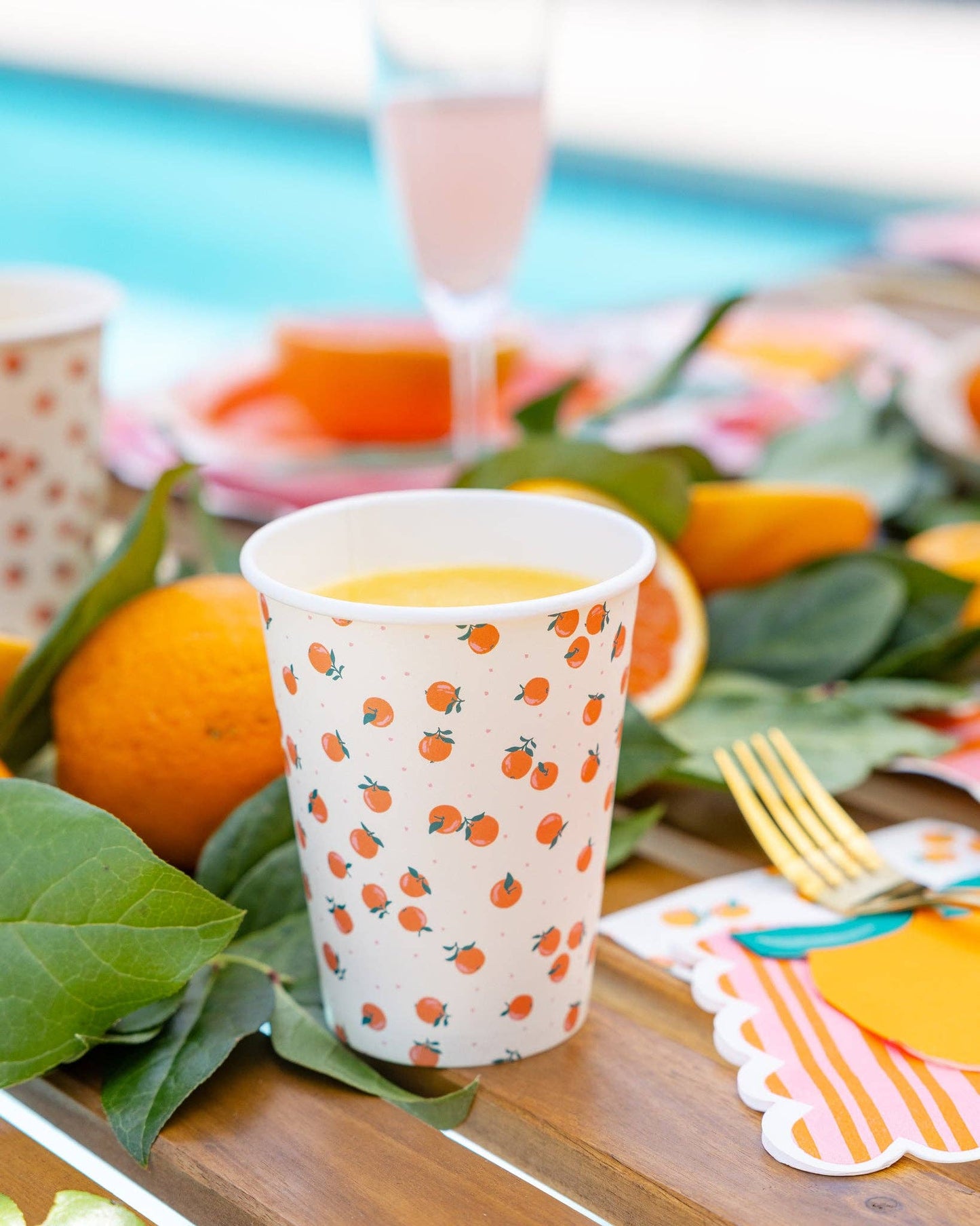 Paper cup with mini oranges and polka dots on a table with oranges and green leaves