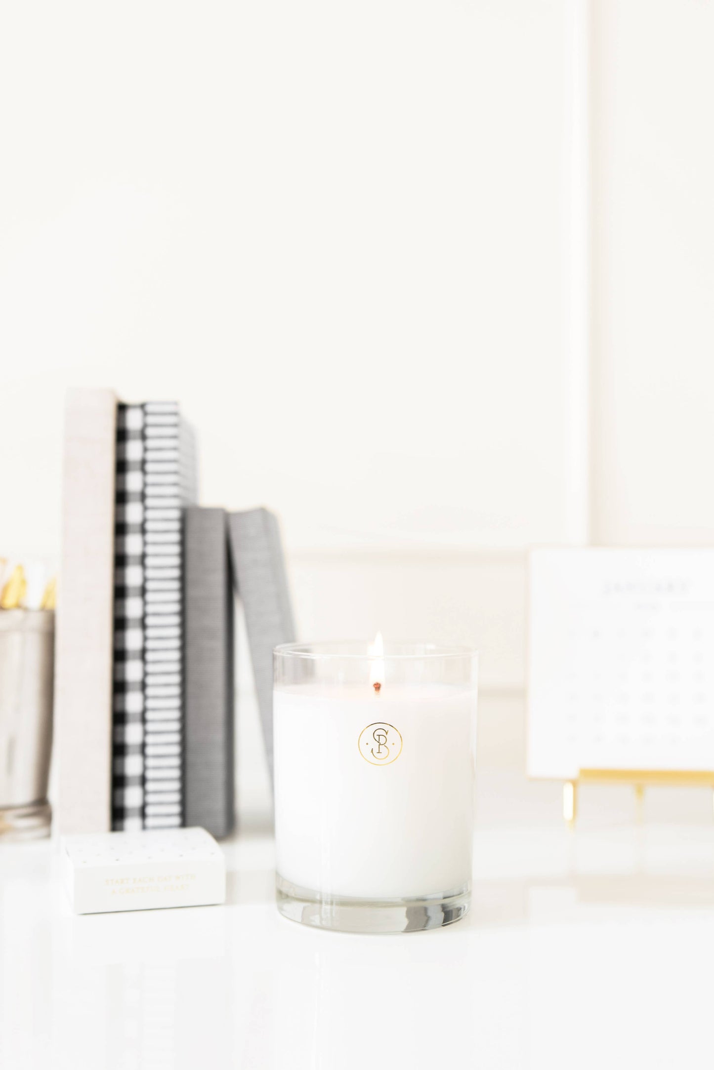 Candle in a glass holder on a white surface with books in the background