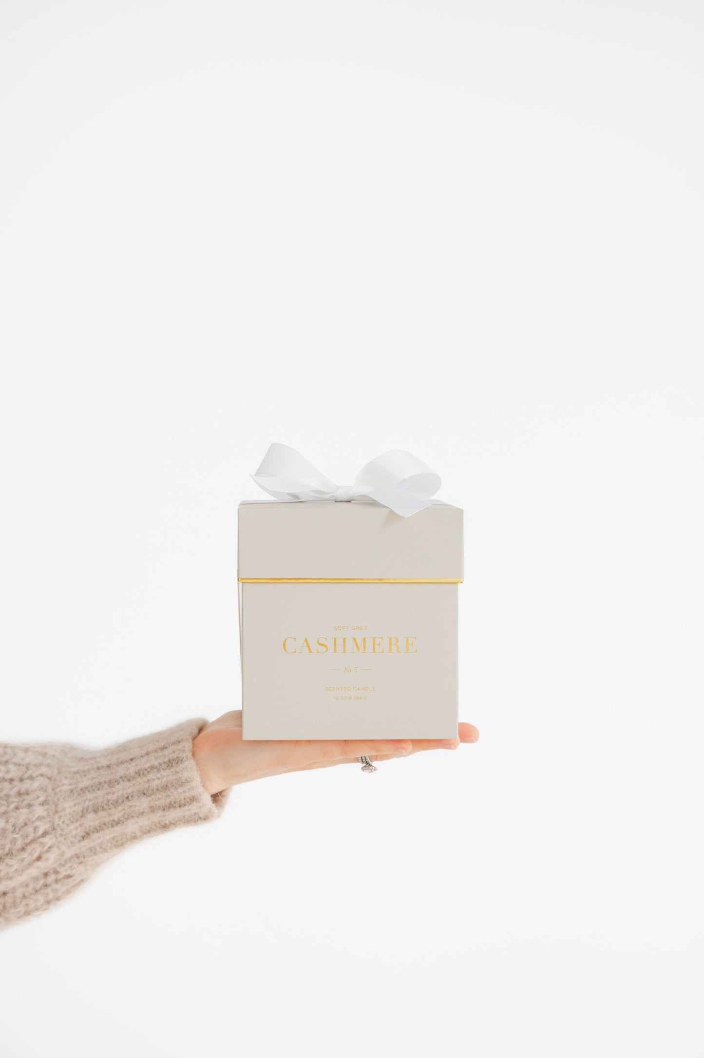 Hand holding a grey candle gift box with 'Cashmere' written on front of the candle box