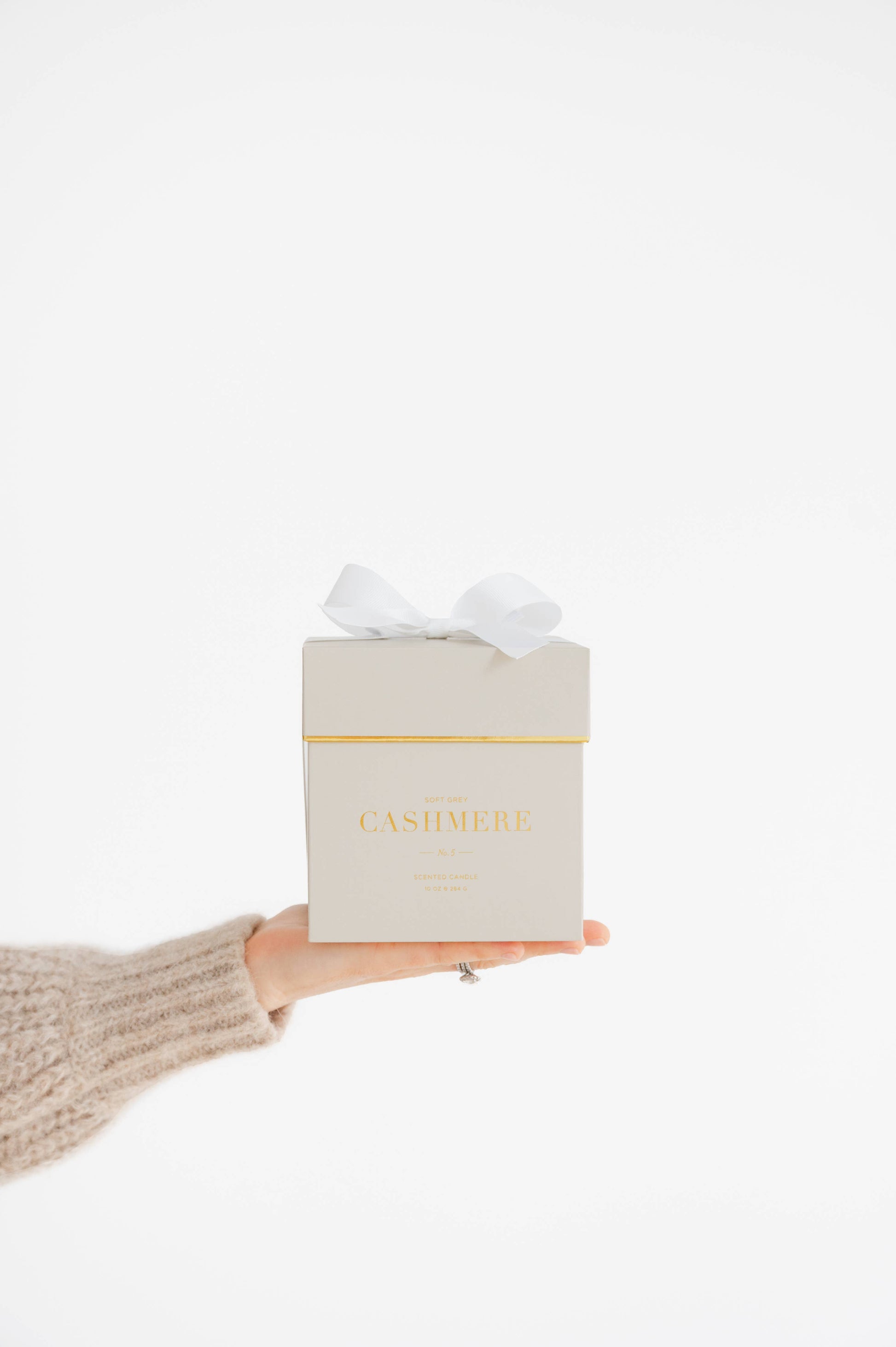 Hand holding a grey candle gift box with 'Cashmere' written on front of the candle box