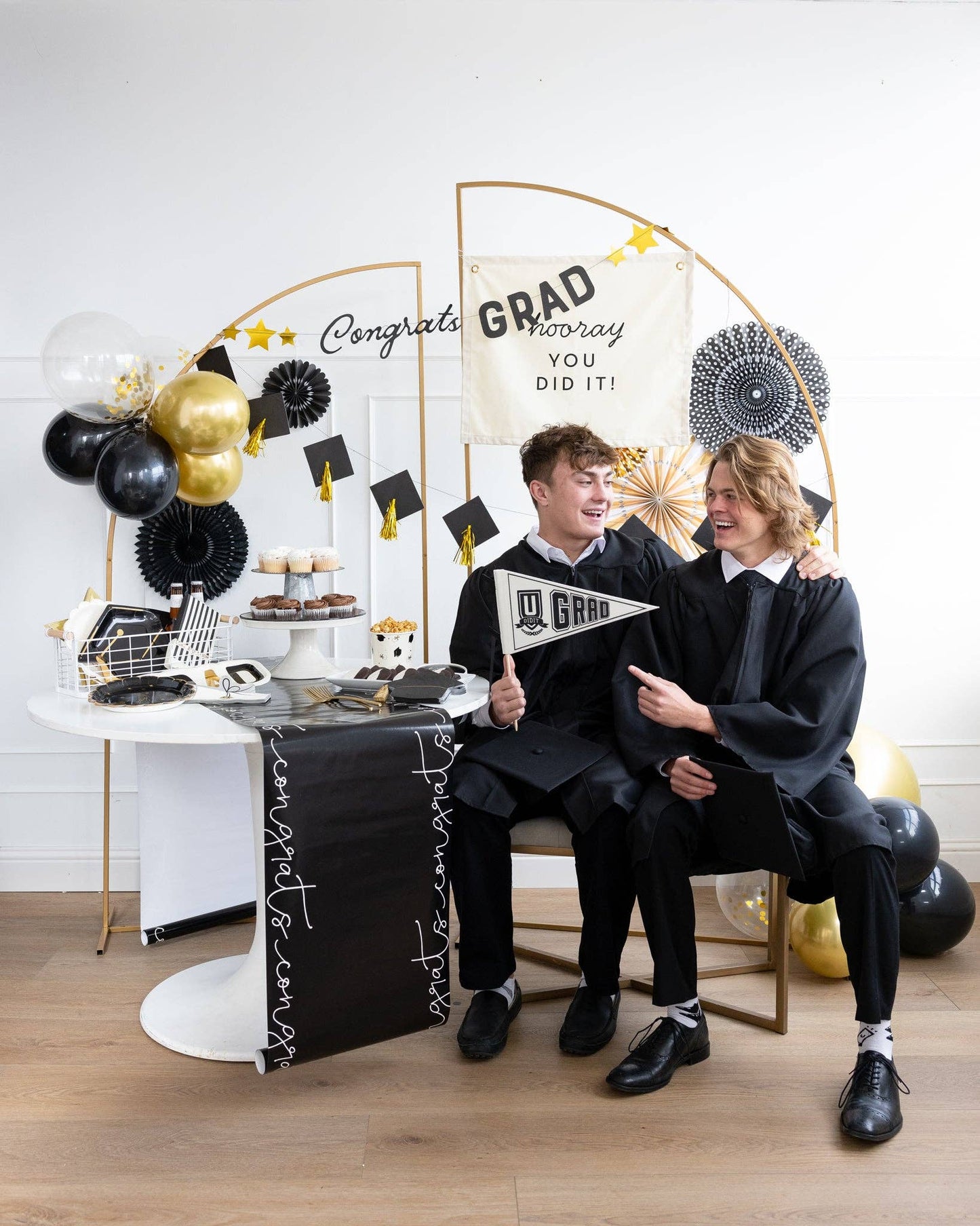 Two graduates at a themed party with decorative balloons and a 'Congrats Grad' banner.