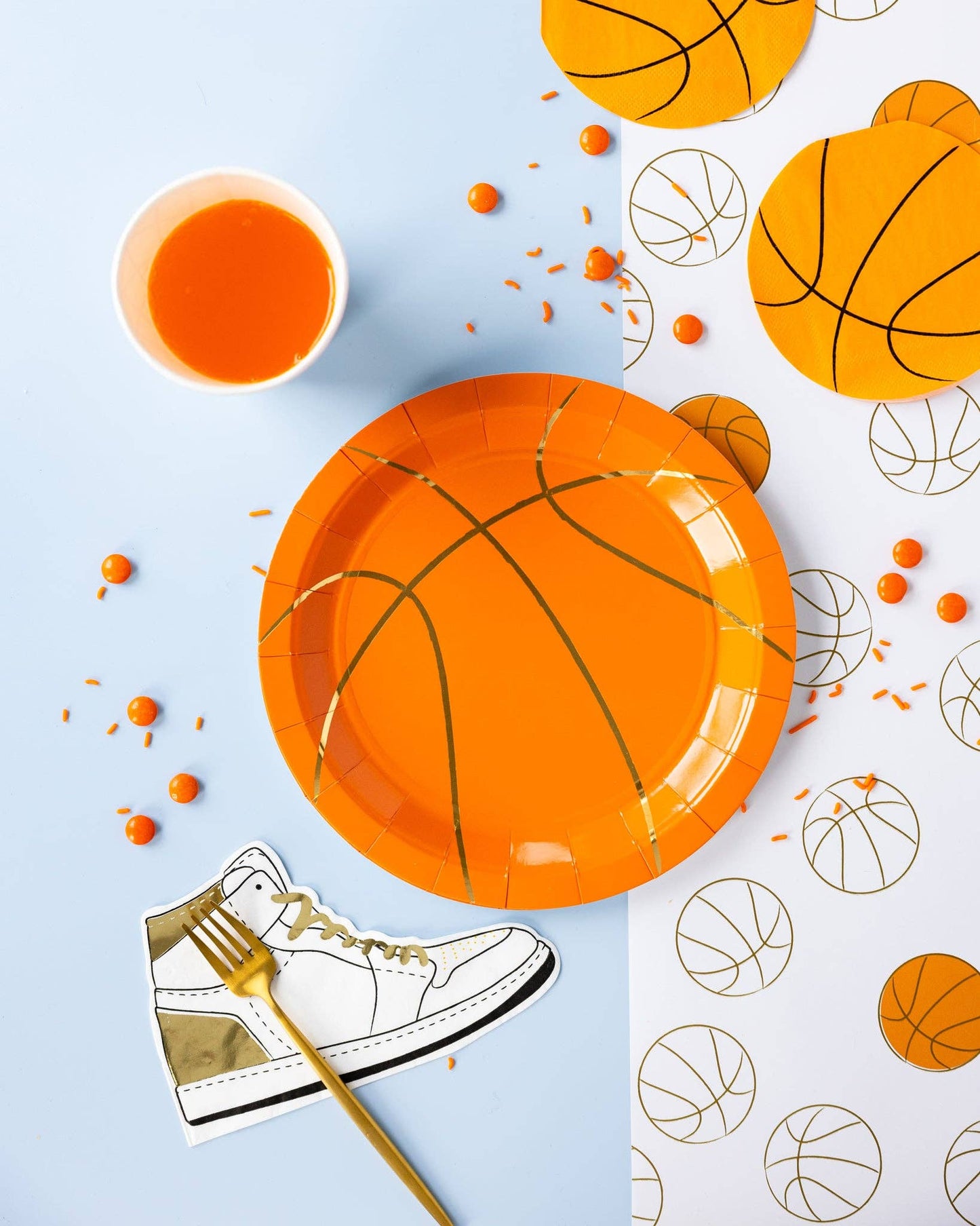 Basketball-themed party supplies including plates, cups and napkins on a light blue background