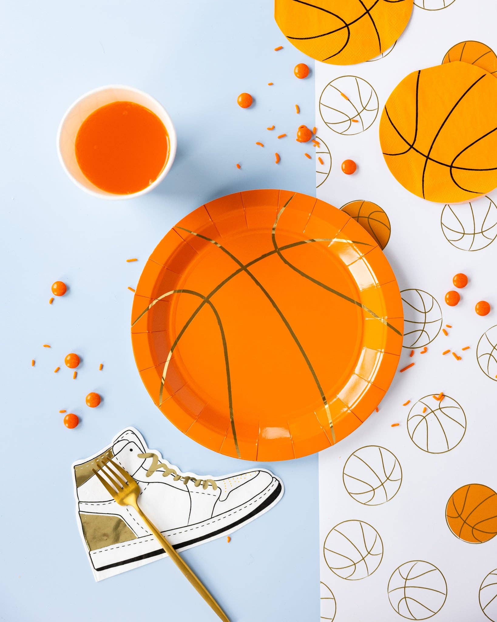 Basketball-themed party supplies including plates, cups and napkins on a light blue background