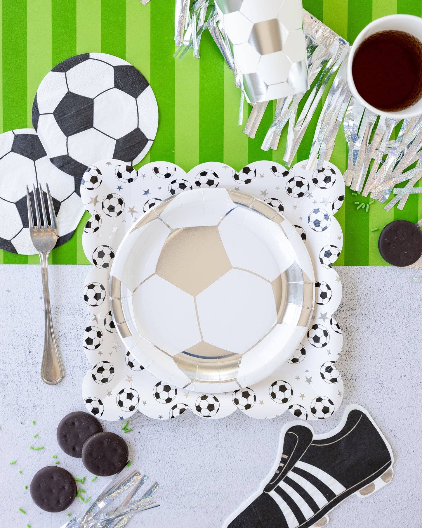 Soccer-themed table setting with plates, cutlery and decorative items on a green and white striped background.
