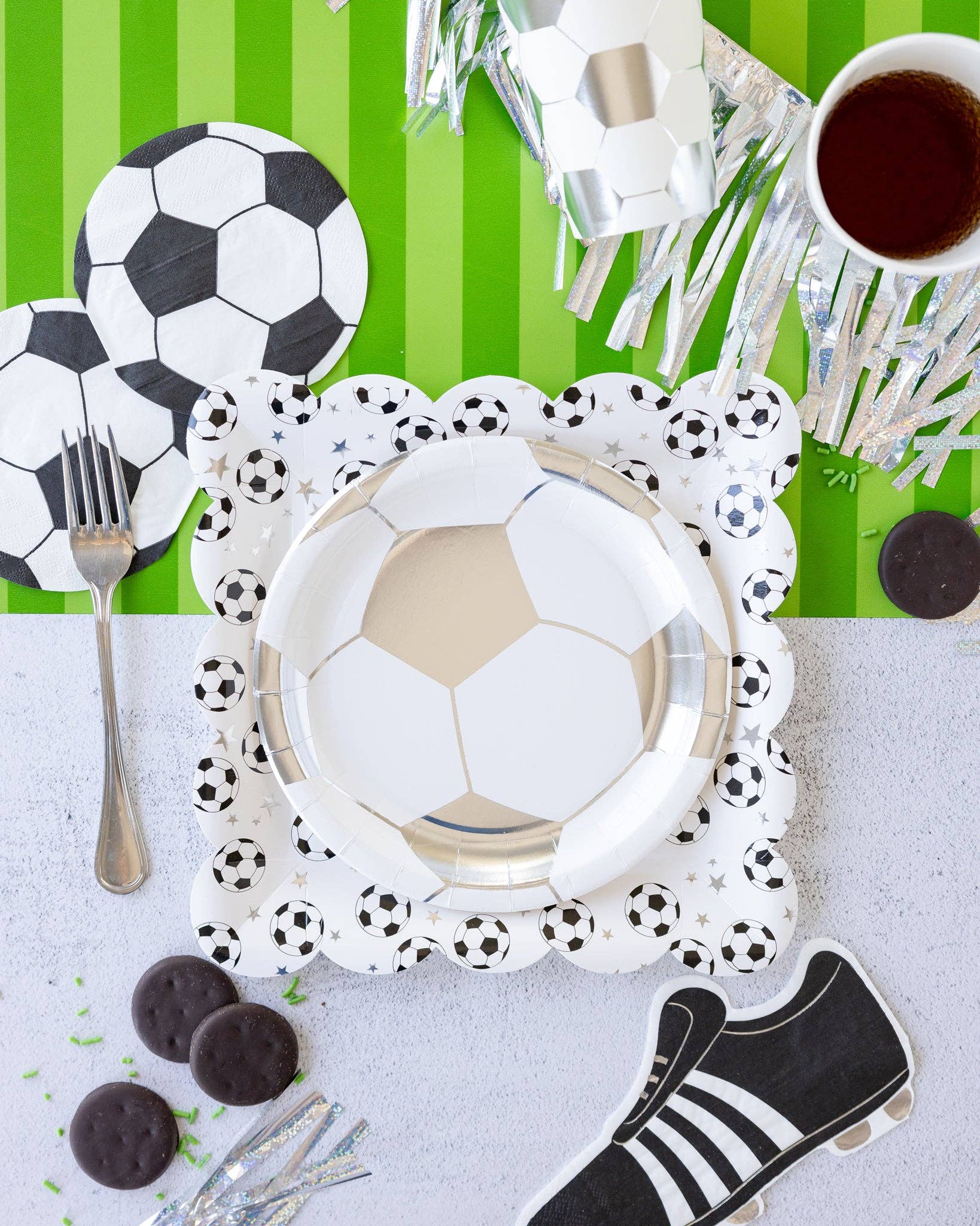 Soccer-themed table setting with plates, cutlery and decorative items on a green and white striped background.