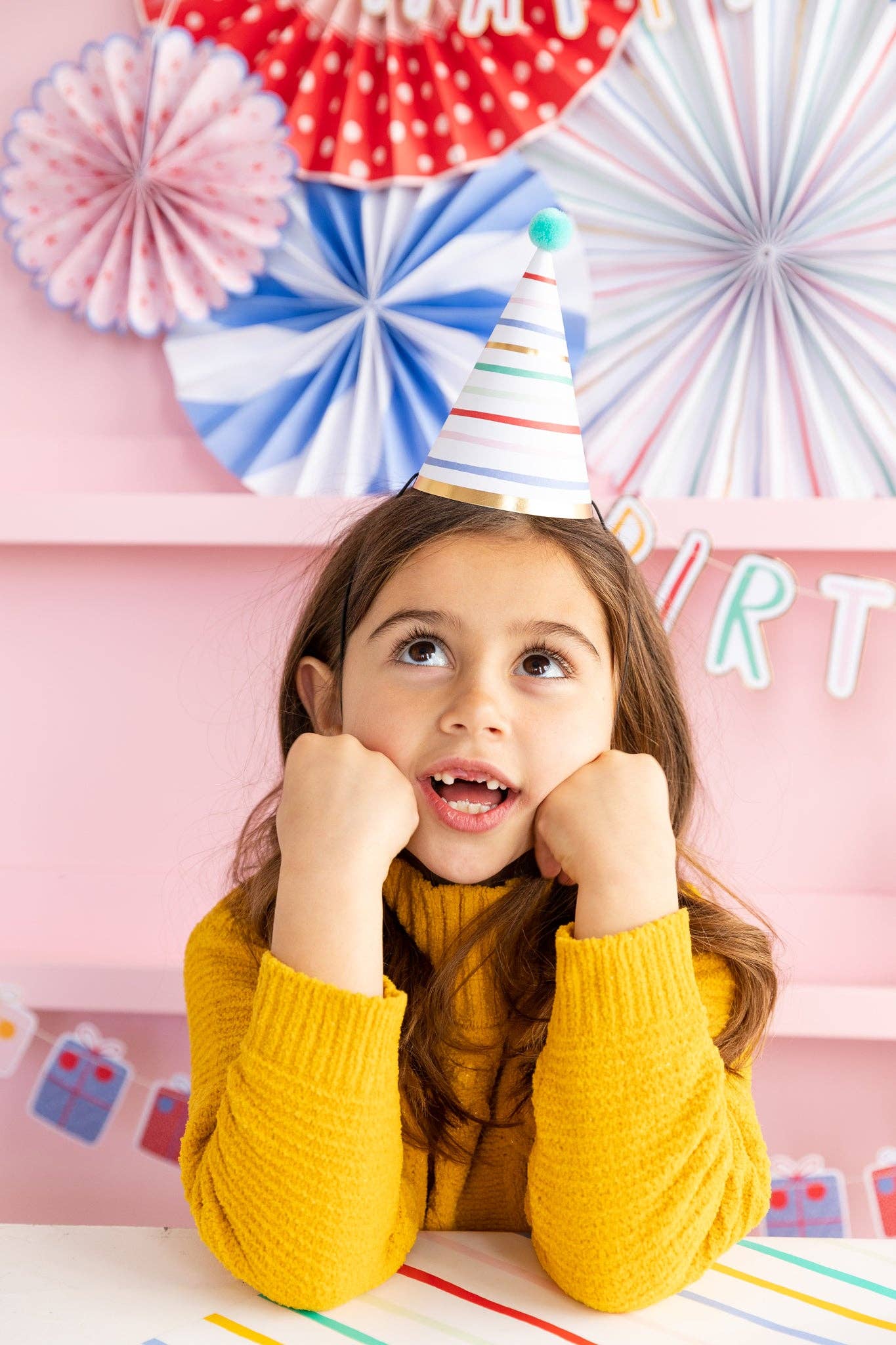 Child wearing a party hat with colorful paper fans in the background