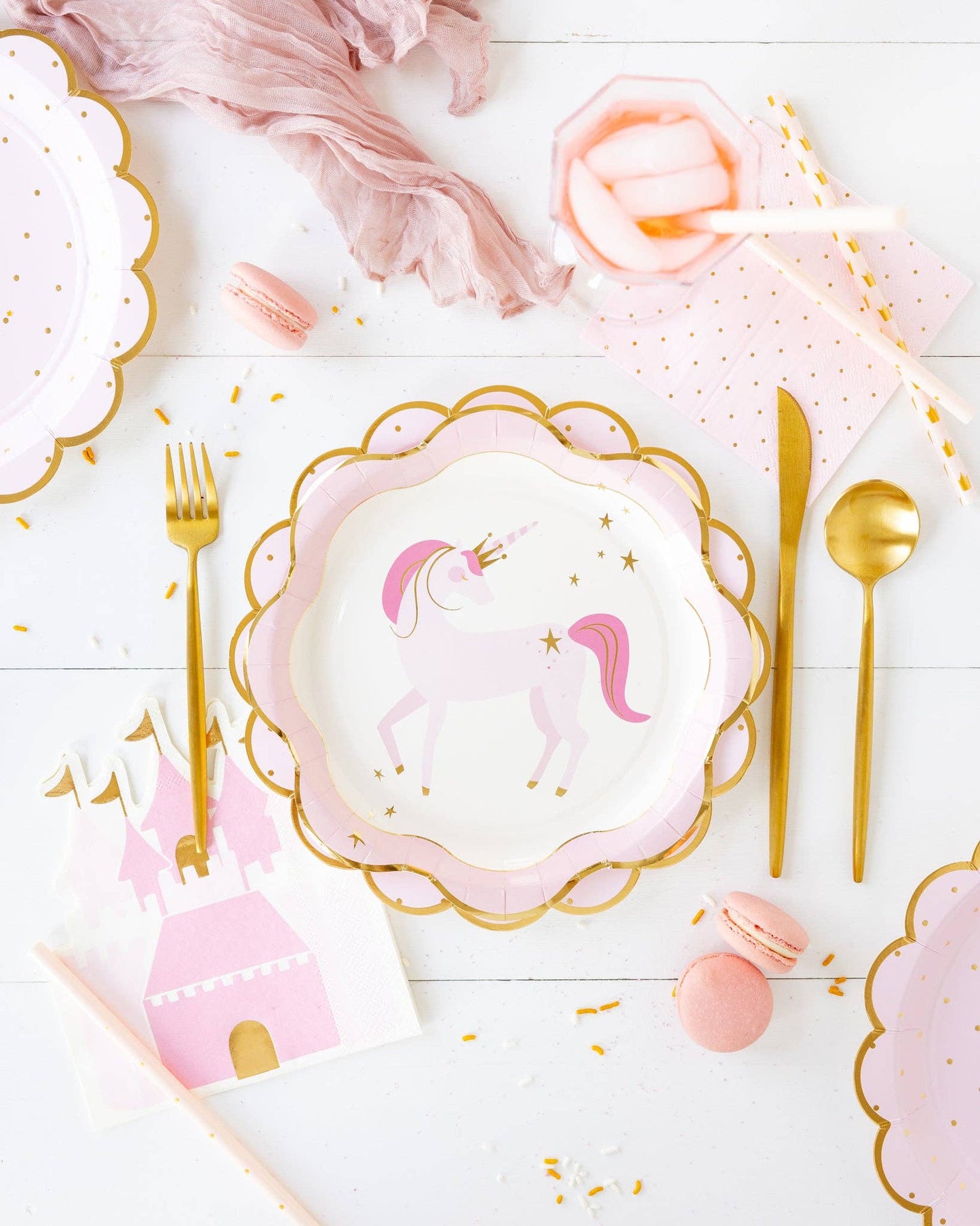 Table setting with unicorn-themed plates, pink castle napkins, and gold cutlery