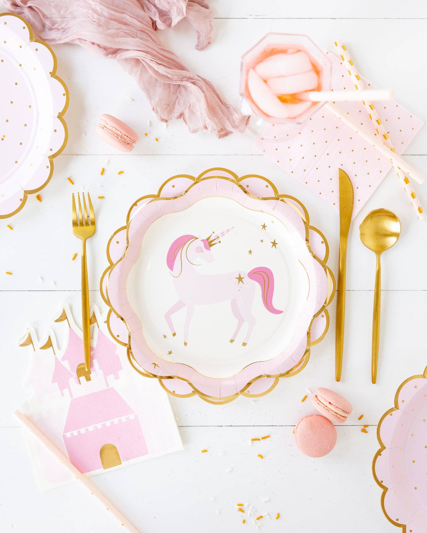 Table setting with unicorn-themed plates, pink castle napkins, and gold cutlery