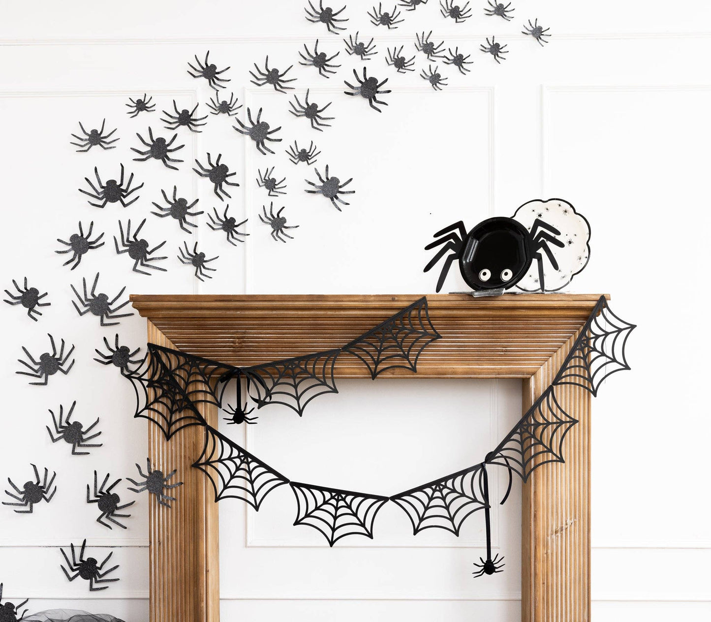 Spider-shaped plate on a mantle with Halloween decorations on a white wall.