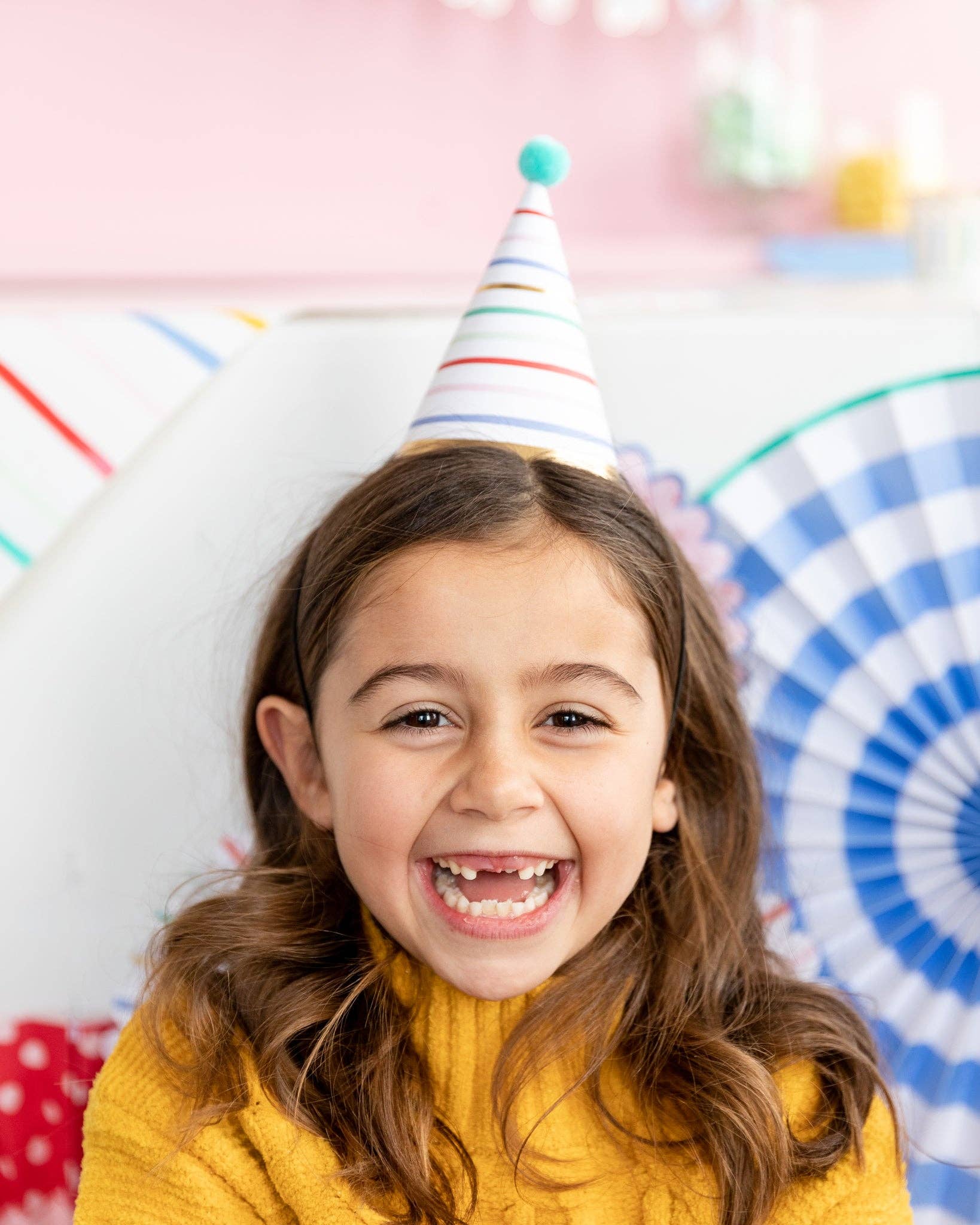 Child wearing a party hat with colorful ribbons against a festive background