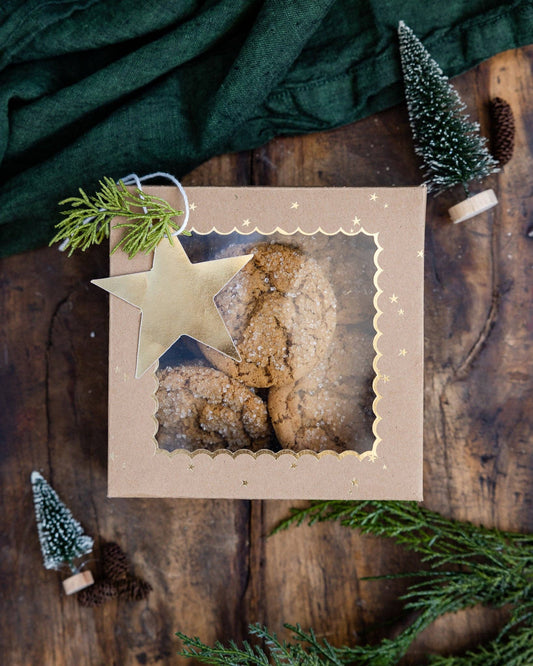 Box of cookies with a star-shaped git tag on a wooden table with Christmas decorations.