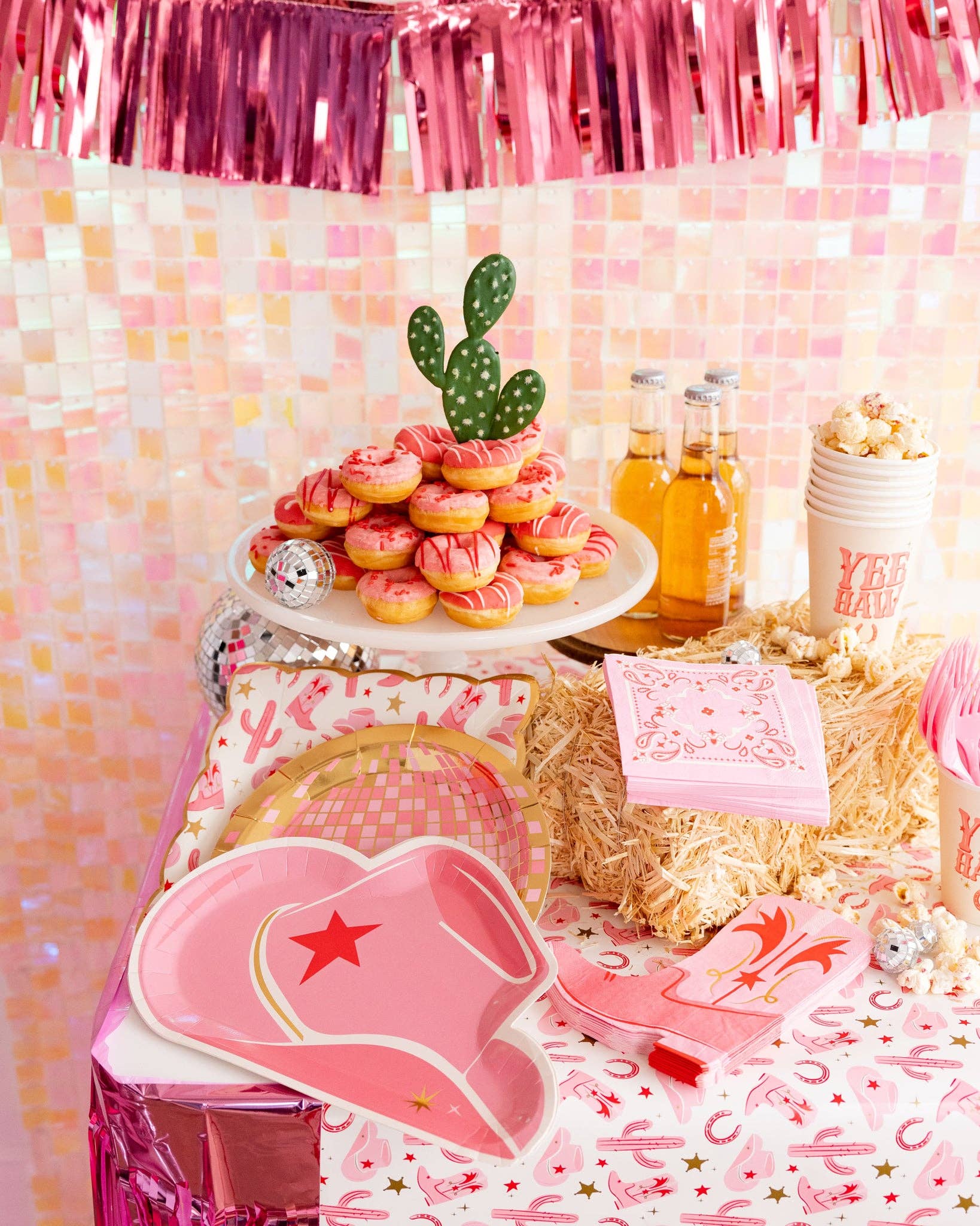 Decorative western table setting with pink cowboy hats, donuts and a cactus-themed centerpiece against a pink and white checkered wall.