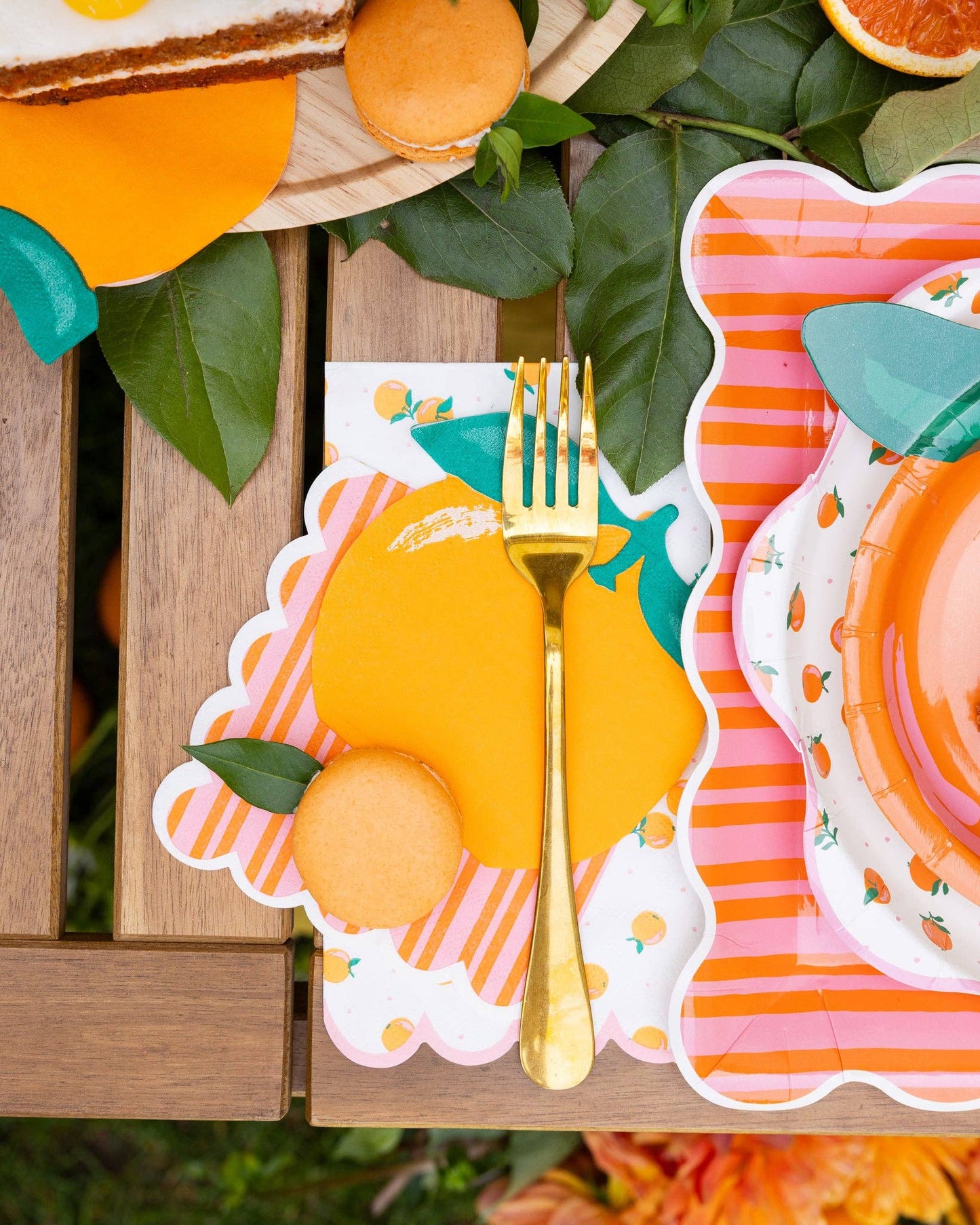 Colorful table setting with orange-themed plates, napkins and a gold fork on a wooden table.