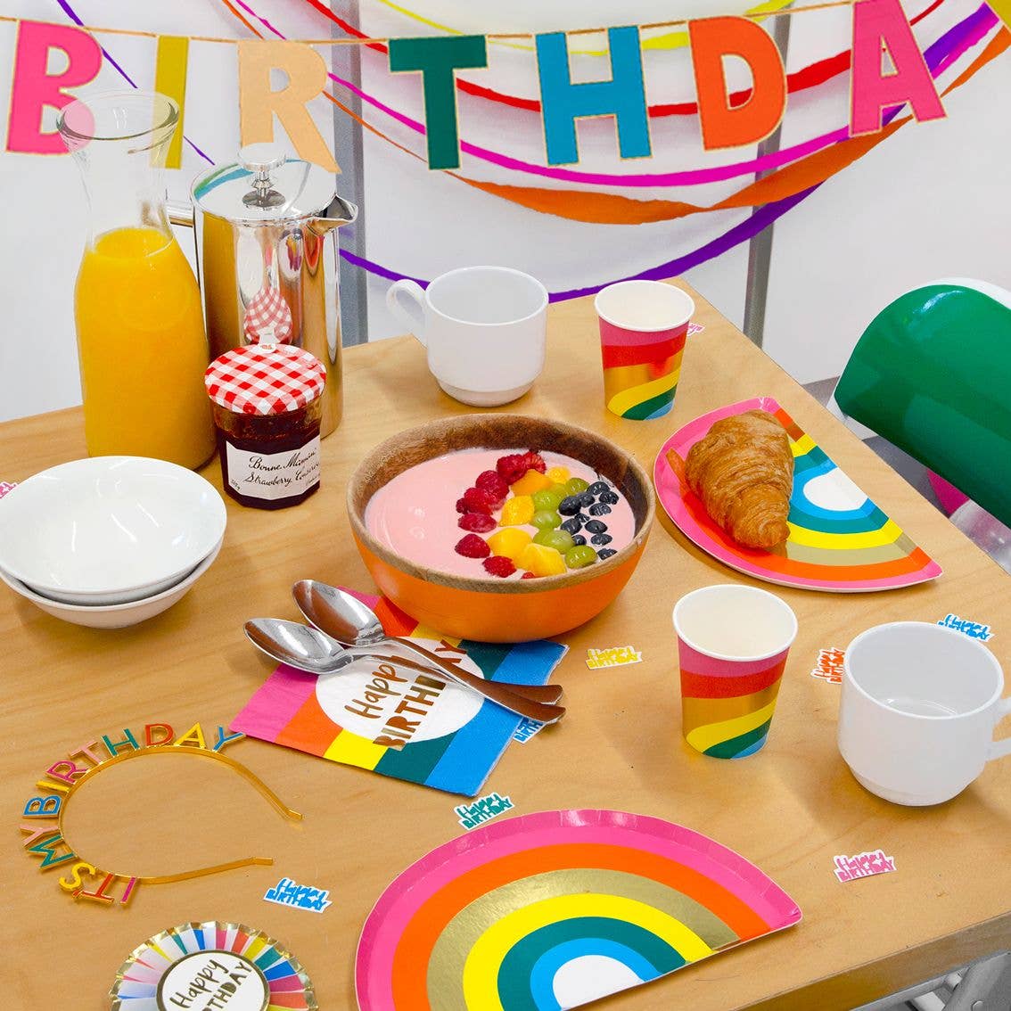 Colorful birthday-themed breakfast party with rainbow plates, colorful decor and a "Happy Birthday" banner in the background.