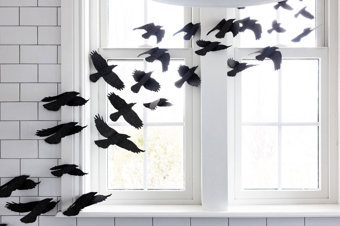 Closeup image of bathroom window adorned with black glittered ravens as Halloween decor.