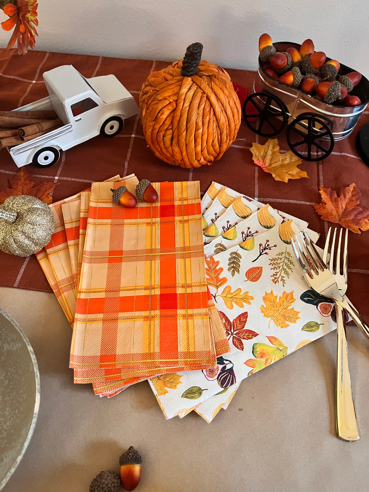 Image of 2 printed napkins, one with a seasonal fall pattern and the other with an orange plaid design