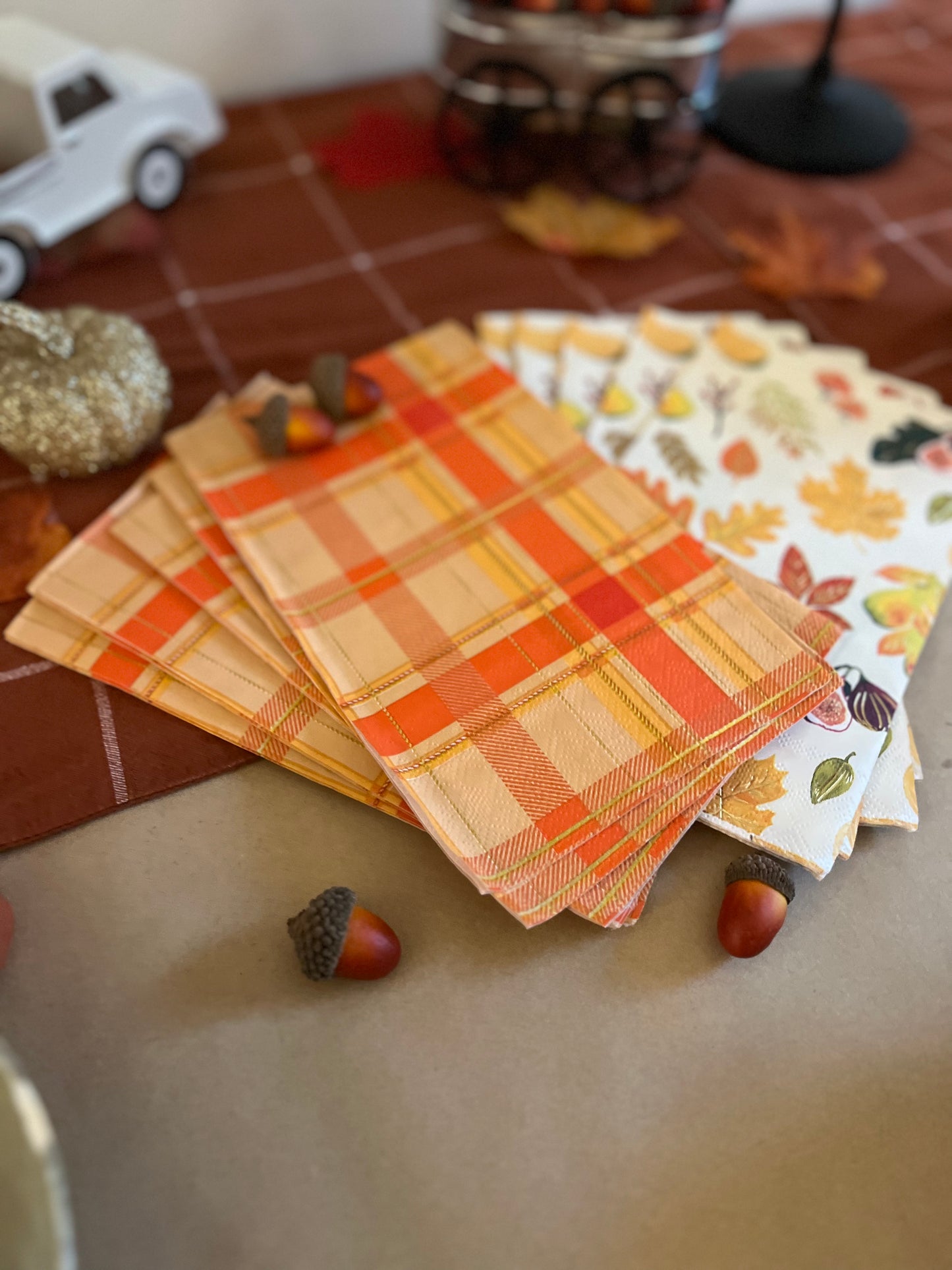 Image of 2 printed napkins, one with a seasonal fall pattern and the other with an orange plaid design