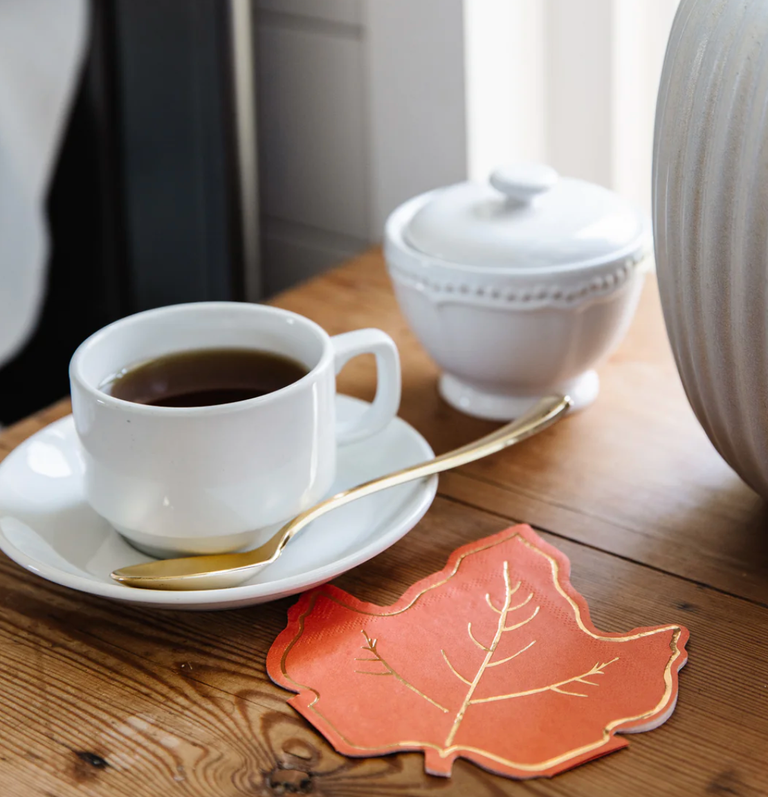 Image of an orange maple leaf napkin next to a cup of coffee.