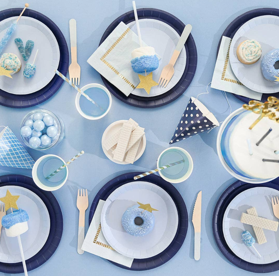Table setting with blue and white plates, napkins, and utensils on a light blue background.