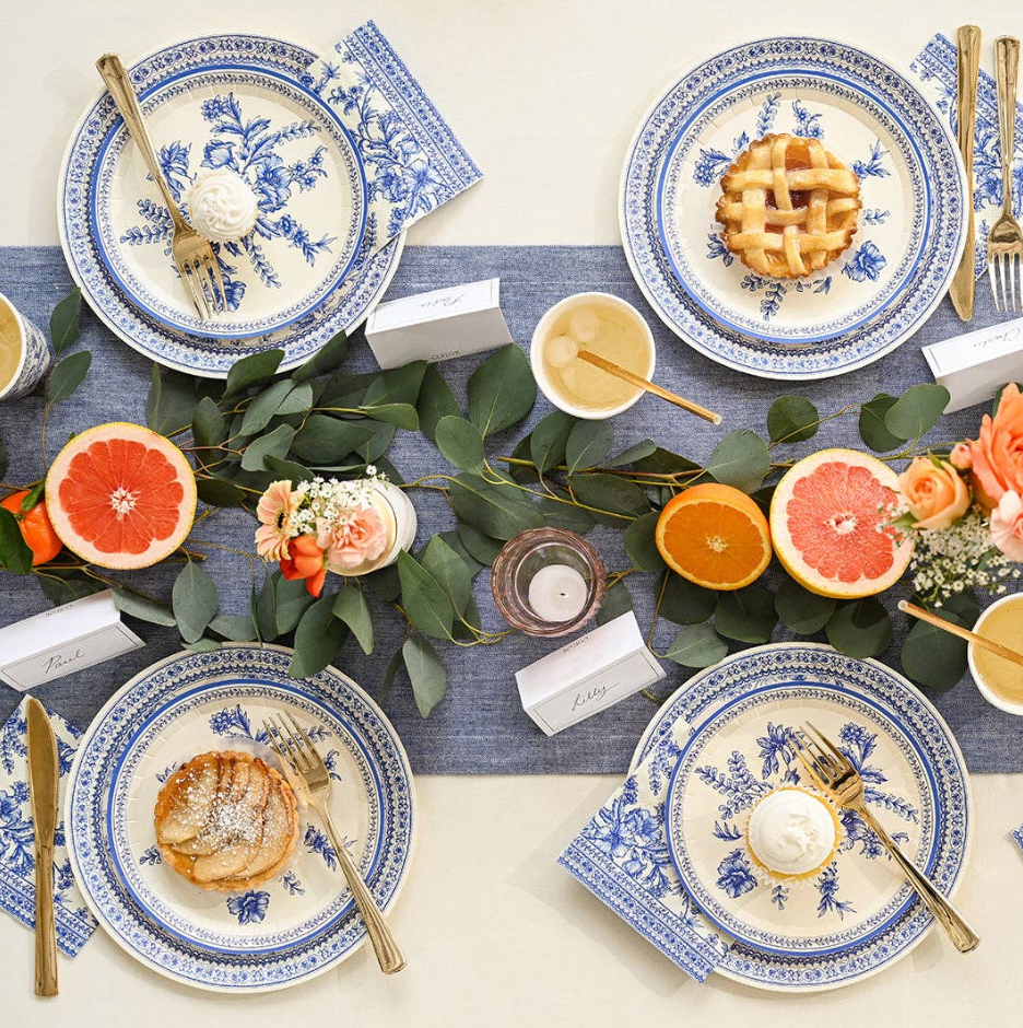 Elegant table setting with blue and white plates, pie, and fruit on a blue tablecloth.