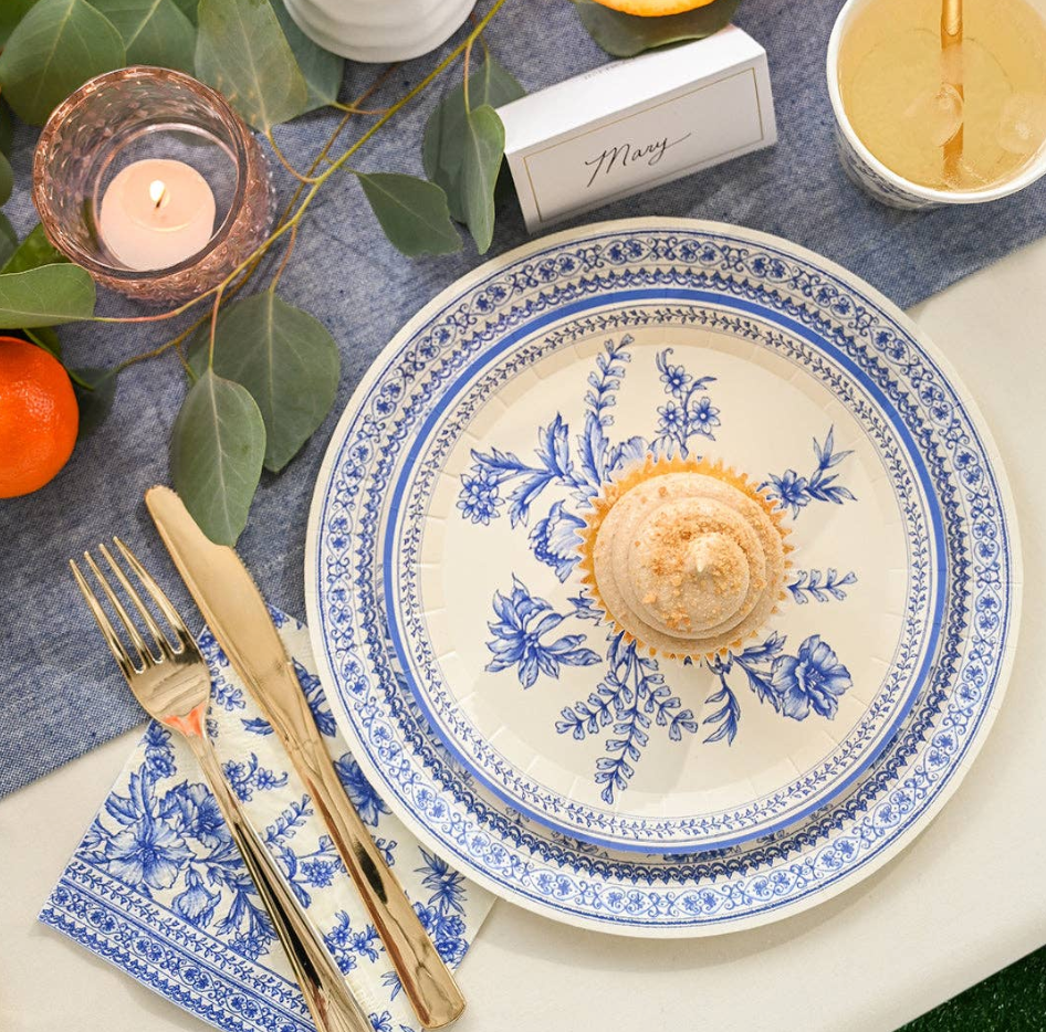 Decorative table setting with a blue and white plate, cupcake, and cutlery on a gray placemat.