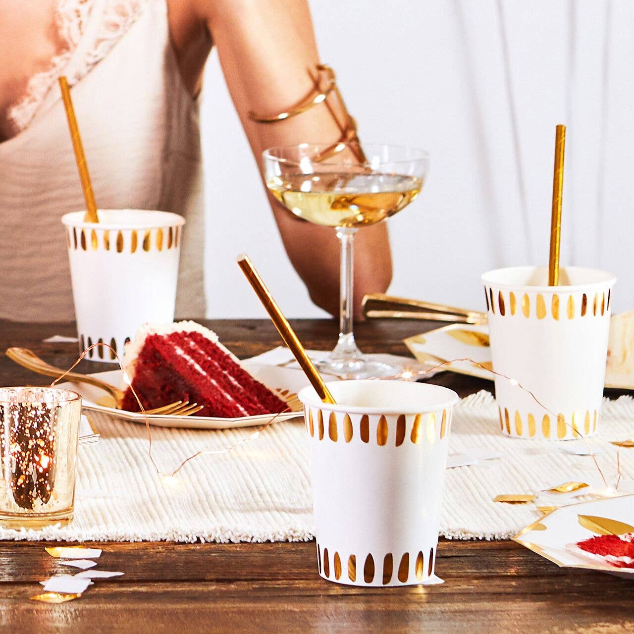 Table setting with gold-trimmed cups, gold straws, a slice of red velvet cake, and a glass of white wine.