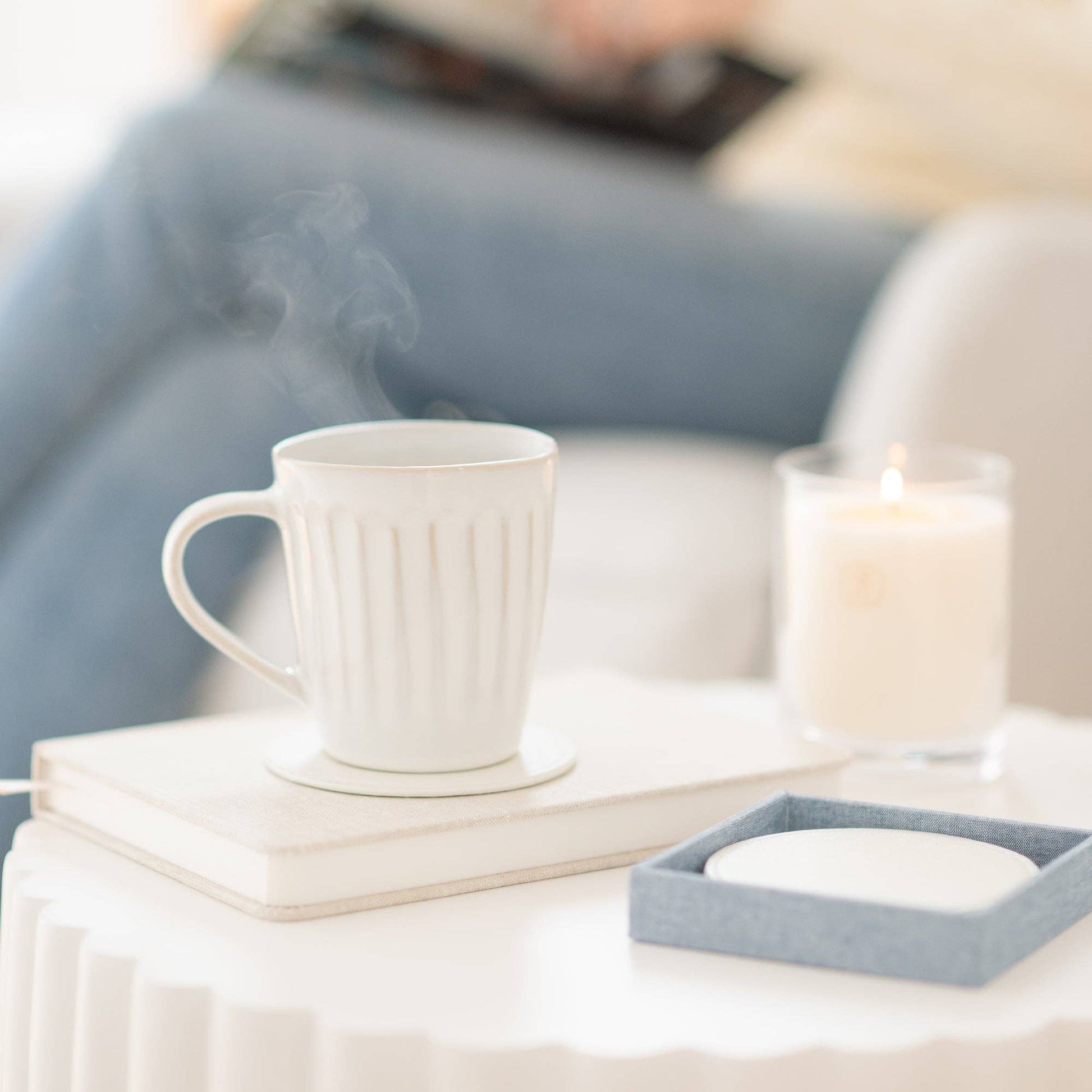 Steaming mug on a coaster on a table with a candle and books in a cozy setting