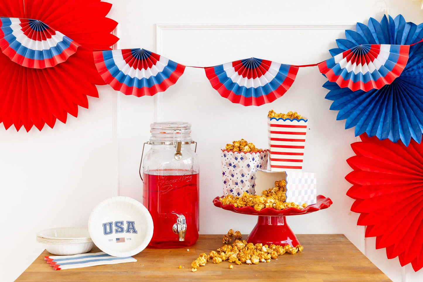 Decorative setup with red, white and blue paper fans and a table with snacks and drinks.