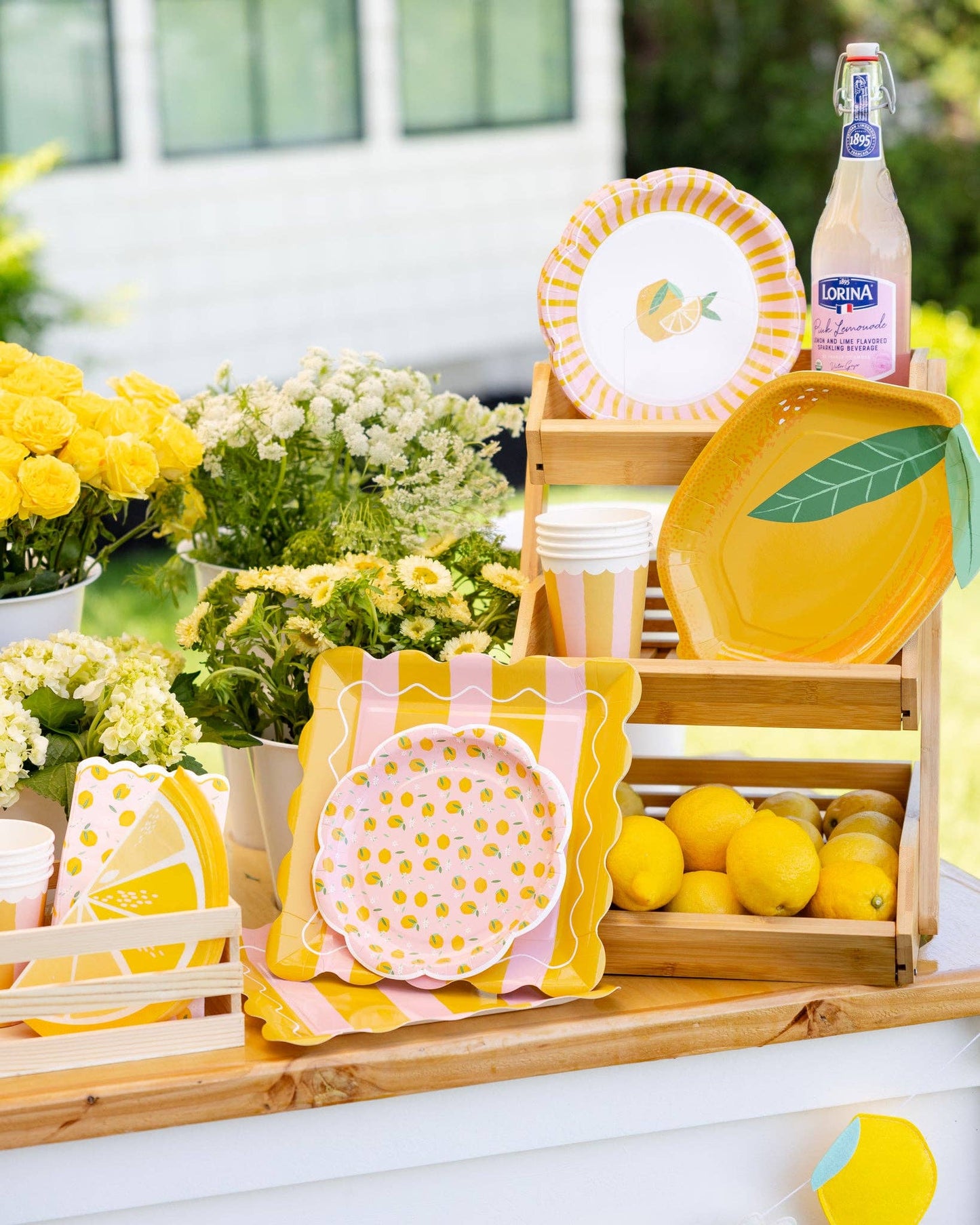 Decorative table setting with flowers, lemon-themed plates and a bottle of lemonade.