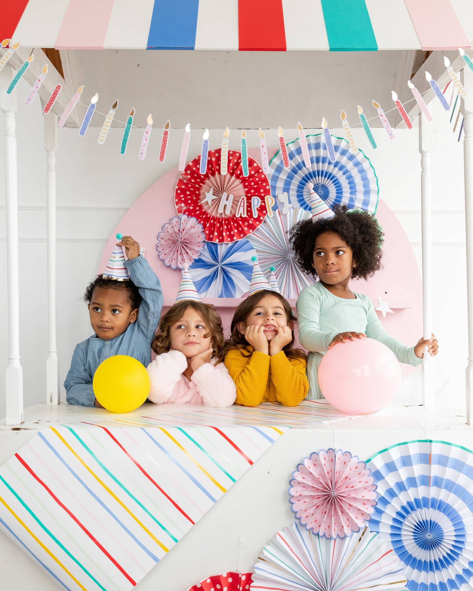 Children celebrating a birthday with colorful decorations and balloons, each wearing a festive party hat