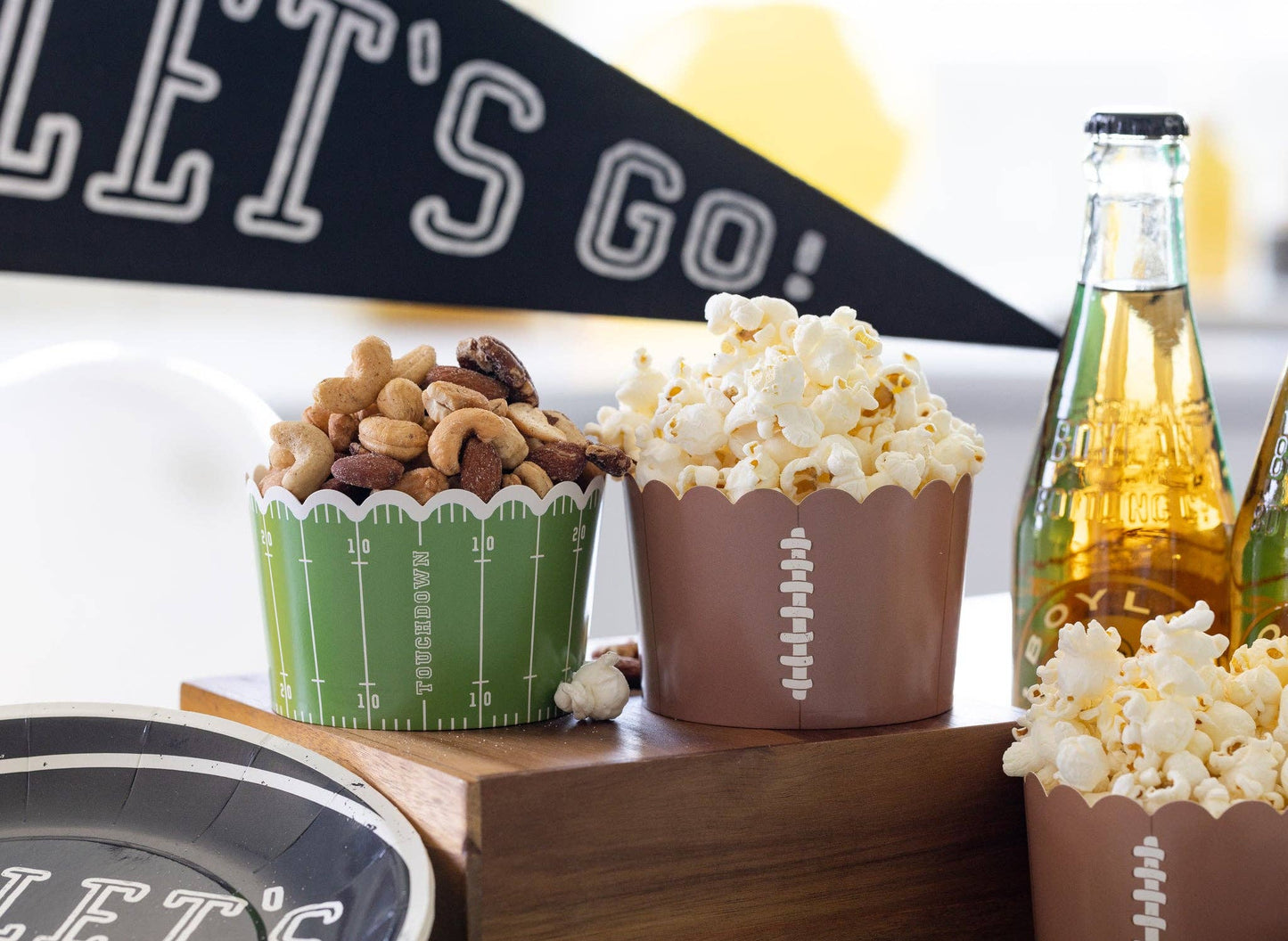 Football food cups with snacks on a wooden tray with a 'Let's Go' banner in the background