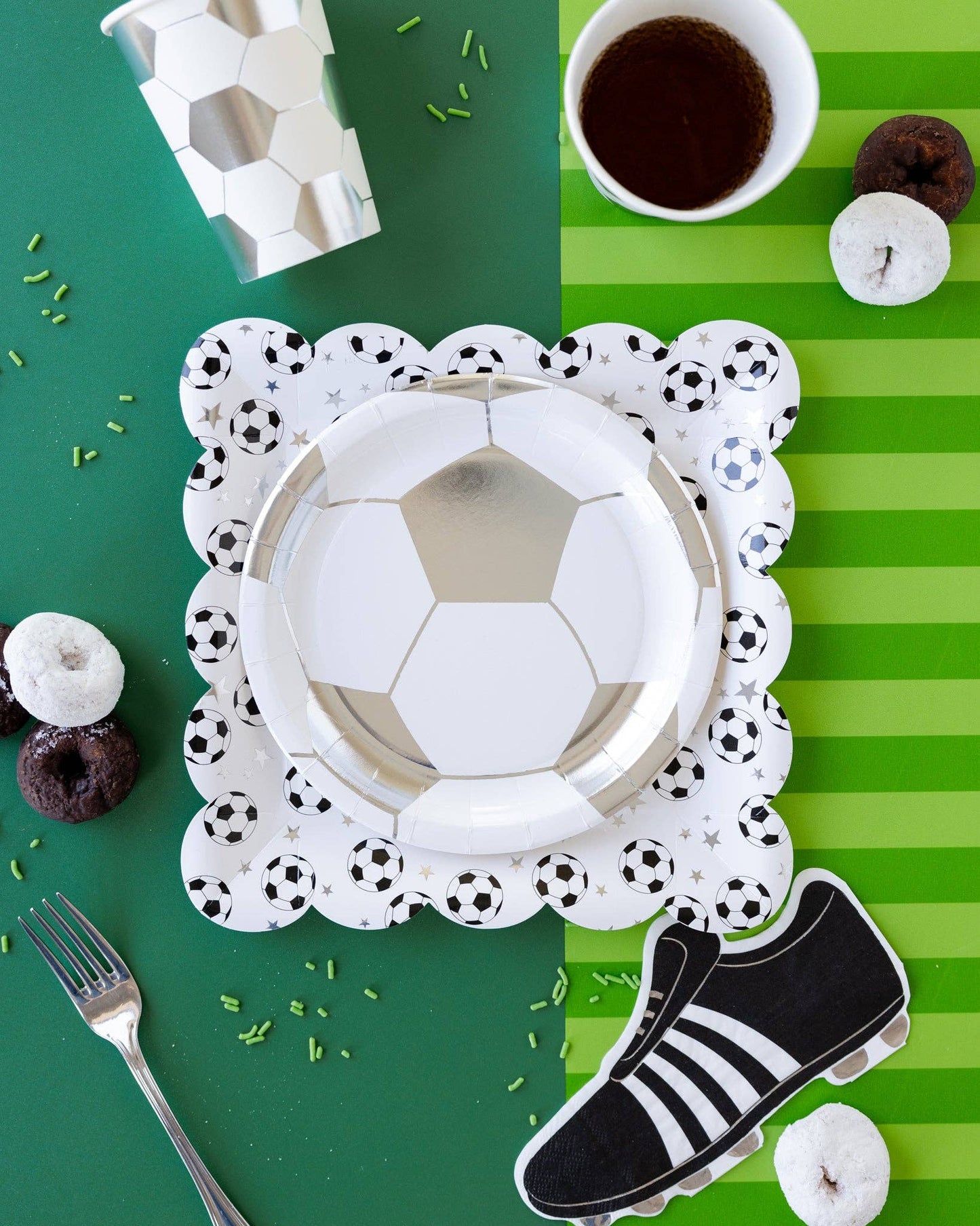 Soccer-themed party setup with paper plates, cup and decorations on a green and white striped background.