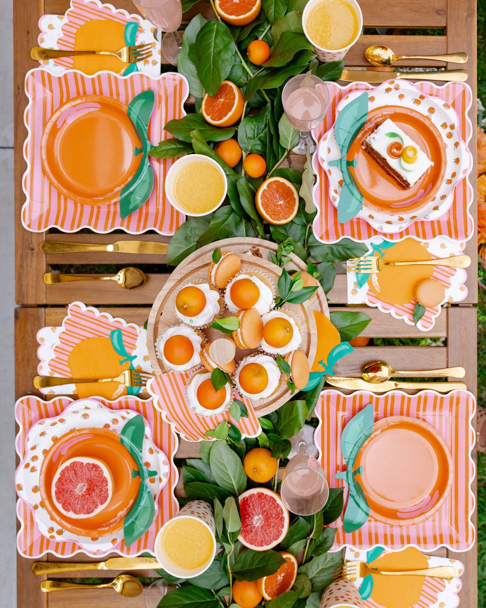 Birds eye view of a citrus-themed tablescape with orange plates, napkins cup and food.
